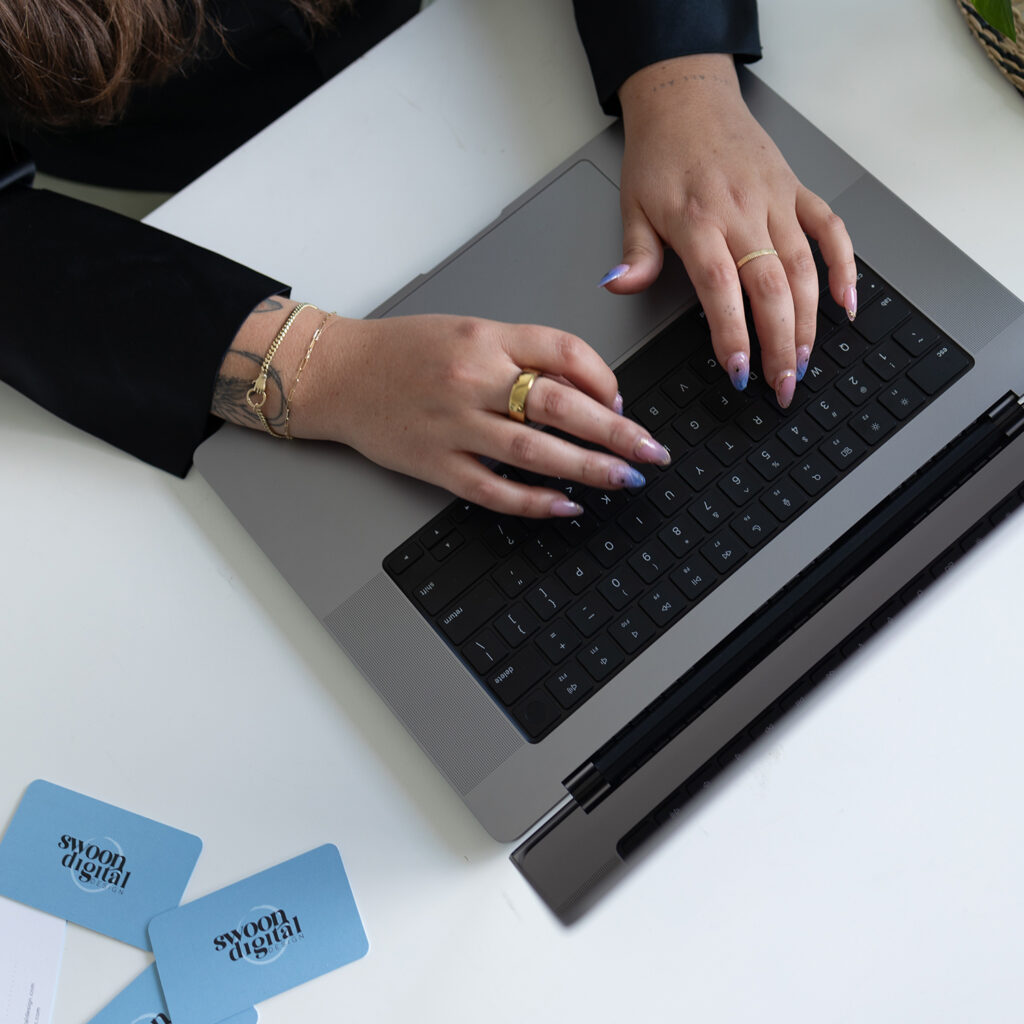 Hands typing on a laptop beside Swoon Digital Design business cards