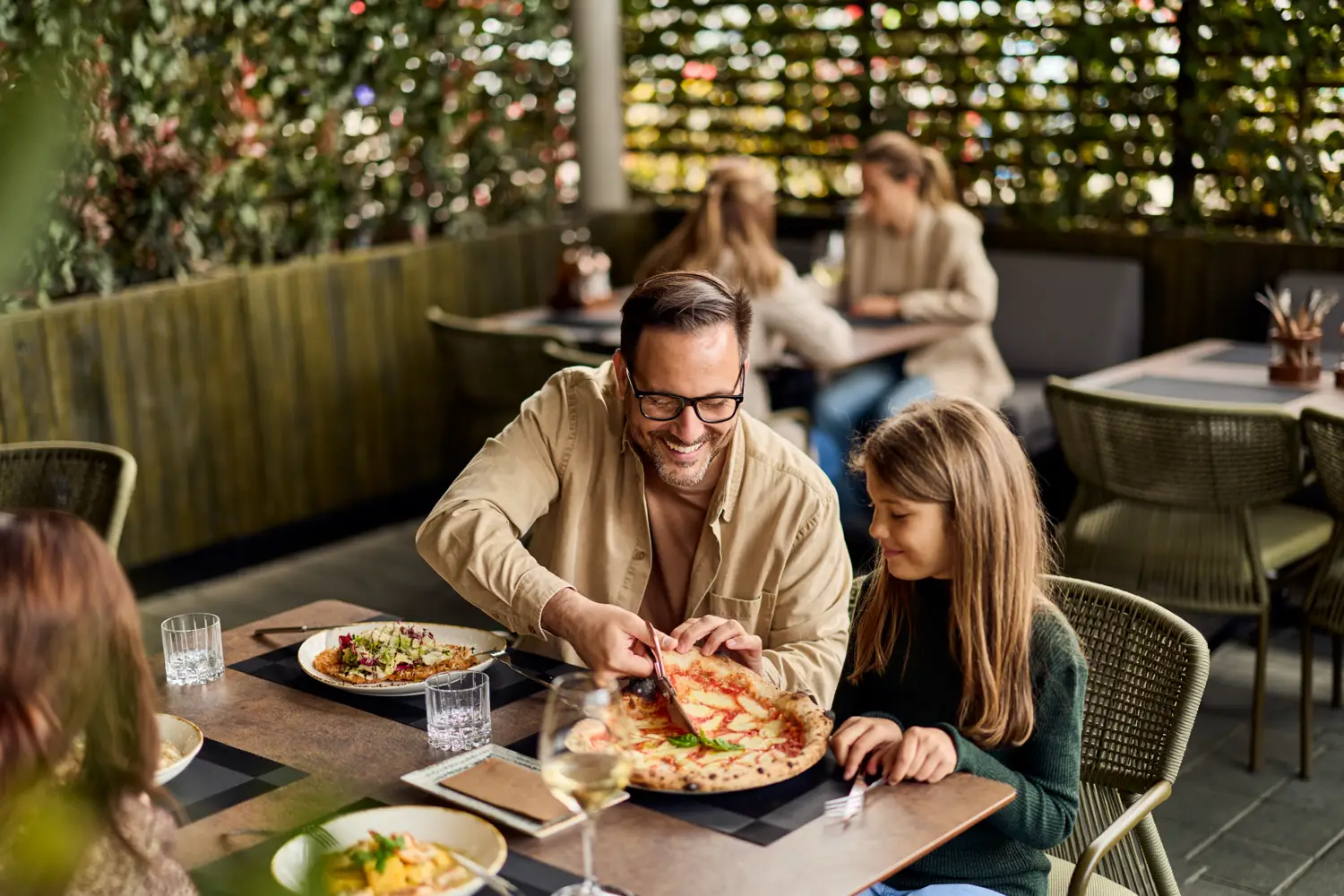 Father and daughter sharing a pizza at a restaurant patio table